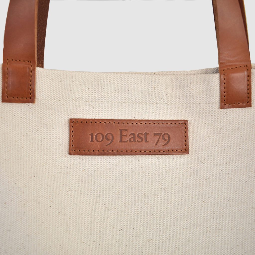 natural canvas tote bag with tan colour PU leather handles and embossed badge