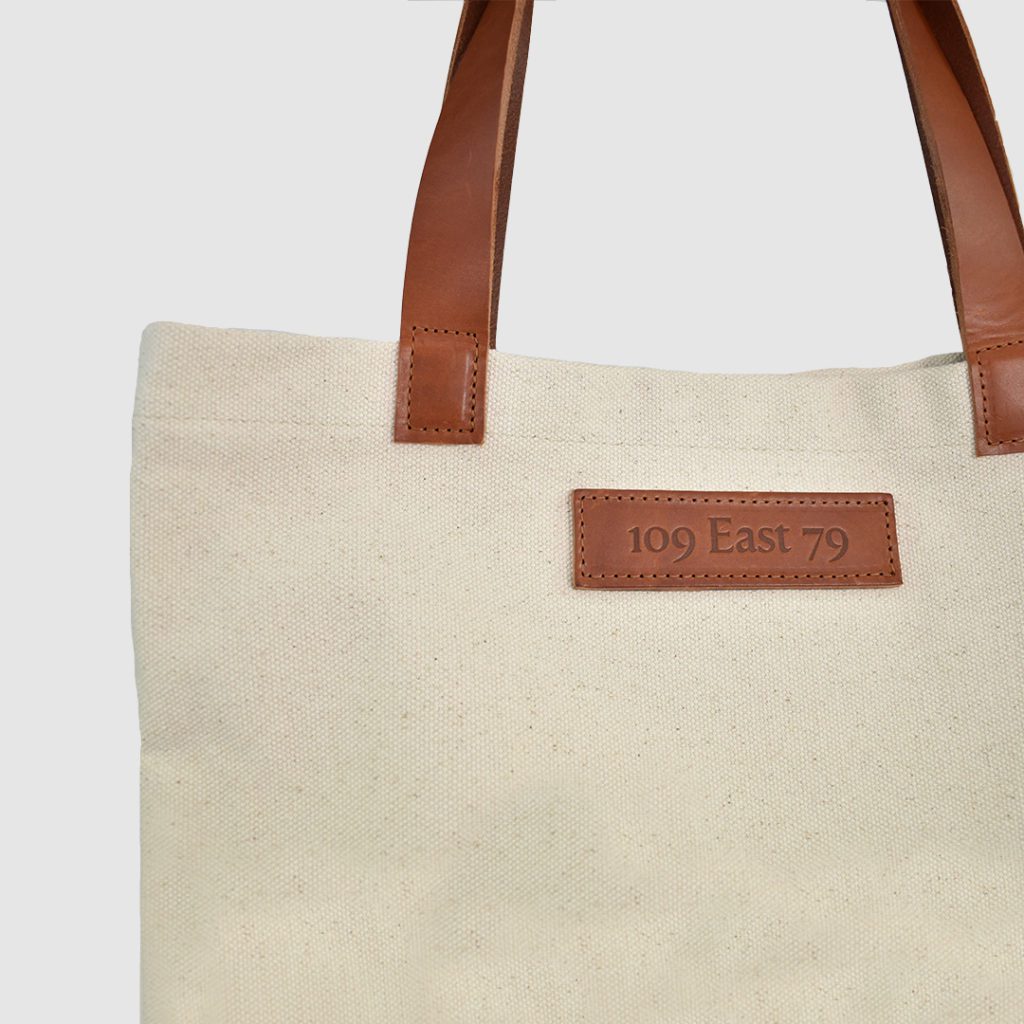 natural canvas tote bag with tan colour PU leather handles and embossed badge