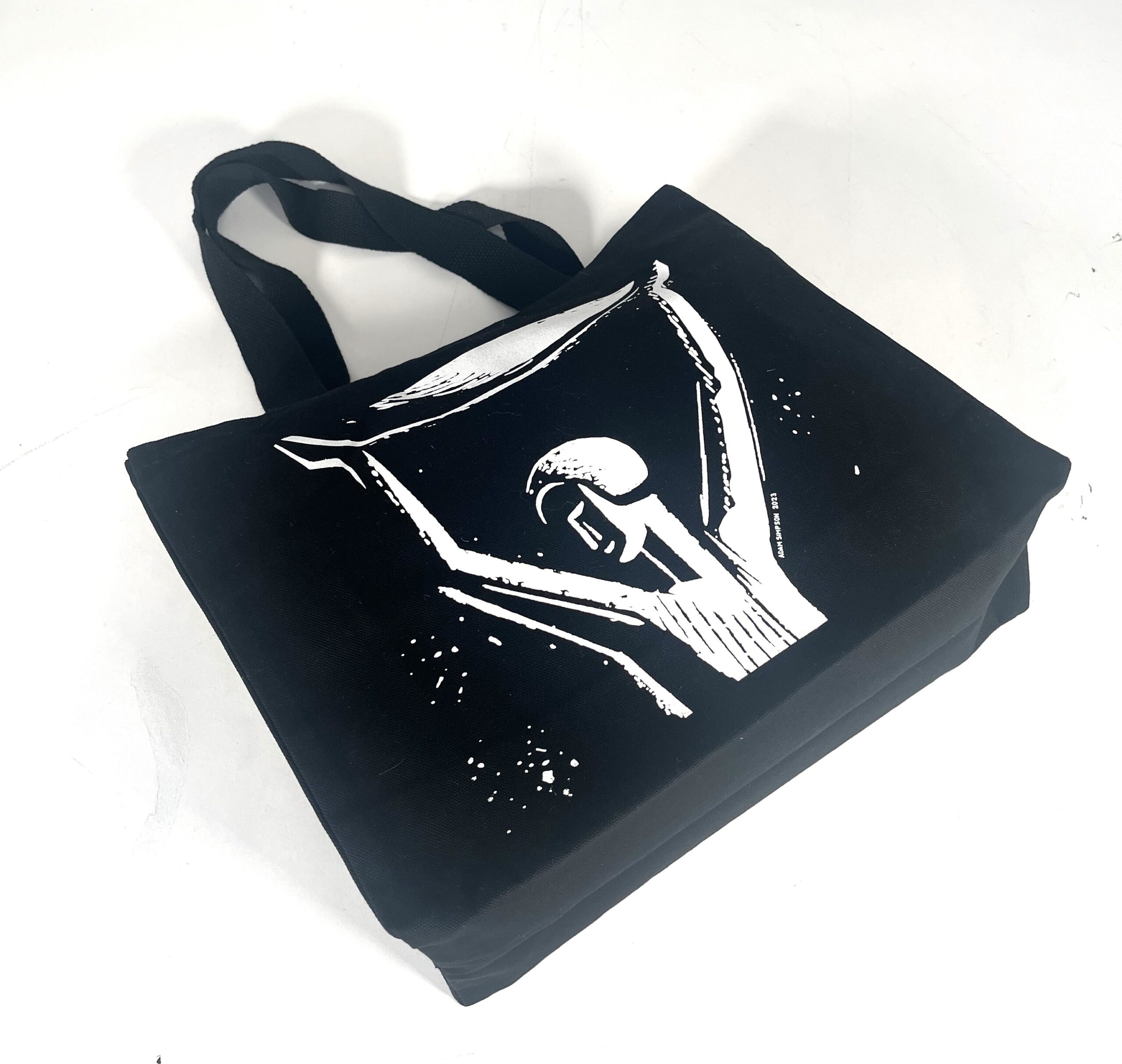 Black square shaped bag lying down with white print of person with arms up in the air from Booker Prize Foundation