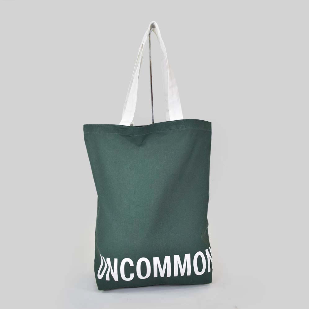 green tote bag with white text that says UNCOMMON on bottom panel of bag