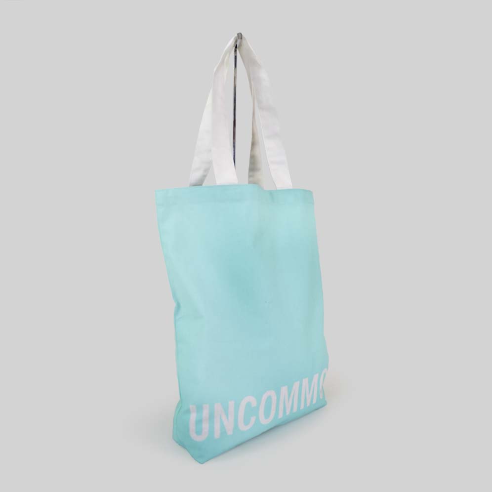 turquoise tote bag with white text that says UNCOMMON on bottom panel of bag