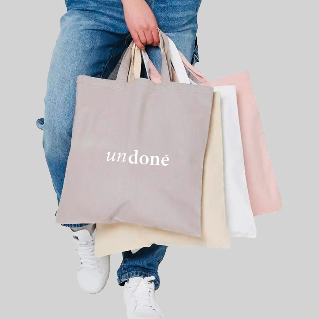 person wearing blue jeans holding four pastel coloured bags with white print on that says 'undone'